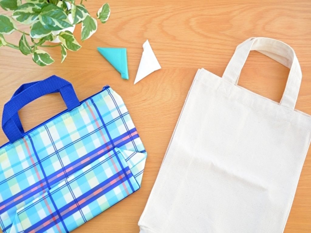 白い布バッグ1つと青いチェック柄の保冷バッグ1つと三角に折り曲げられたビニール袋が2つ