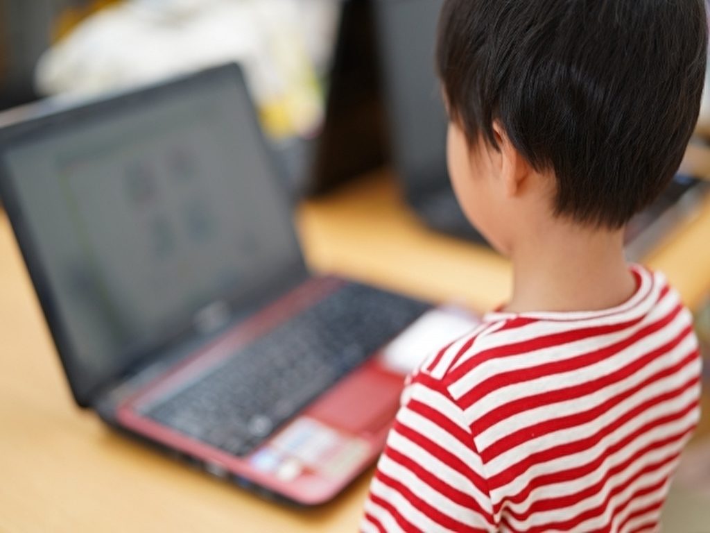 赤と白ボーダーの服を着た子どもがパソコンを見ている